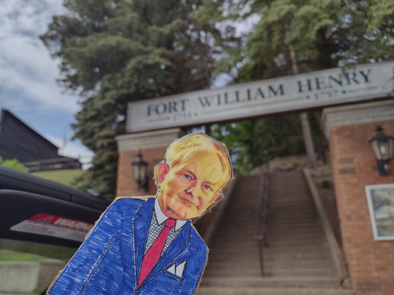 paper doll in front of building fort William henry sign