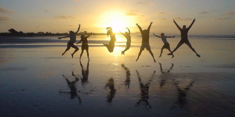 People jumping joyfully on a beach at sunset with their reflections visible.