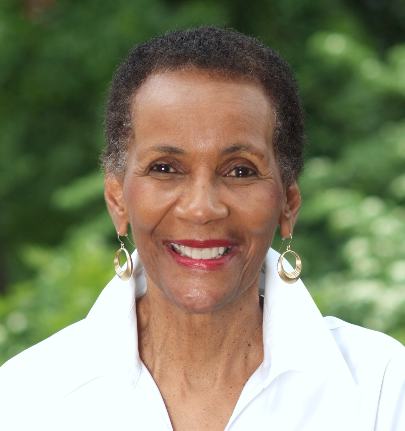 Smiling woman with short hair and hoop earrings outdoors.