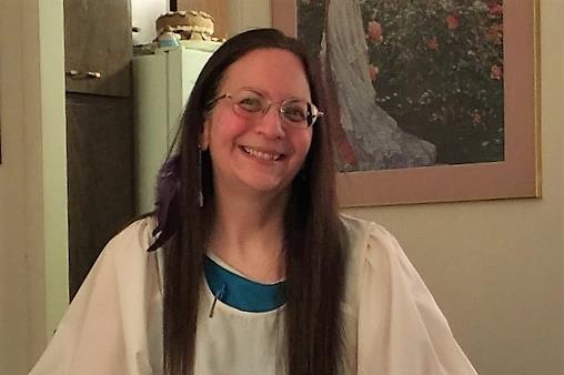 Smiling woman with long hair and glasses in a cozy room.