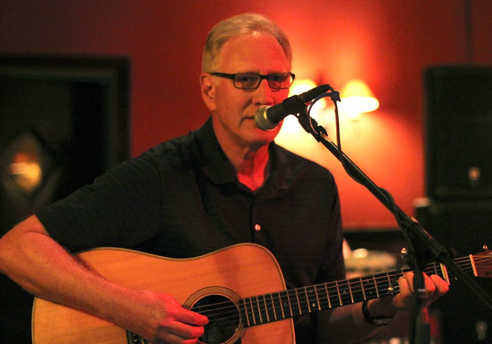 A man playing acoustic guitar and singing into a microphone.