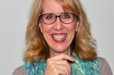 Smiling woman with glasses and a blue scarf.