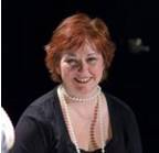 Smiling woman with red hair wearing a pearl necklace and black top.