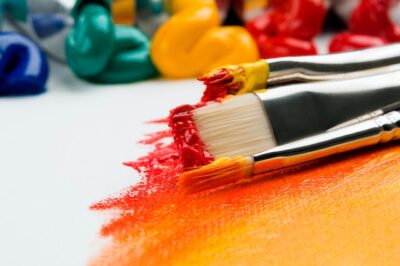 Paintbrushes applying vibrant red and orange paint on a surface.