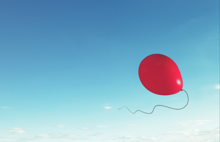 A single red balloon floating against a clear blue sky.
