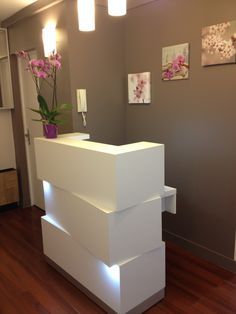 Modern white reception desk with illuminated sections and orchid decoration.