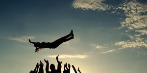 Person crowd surfing with arms raised at sunset.