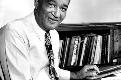 Portrait of a smiling man at a desk with books behind him.