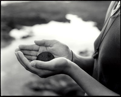 Hands gently holding a small coin near water.