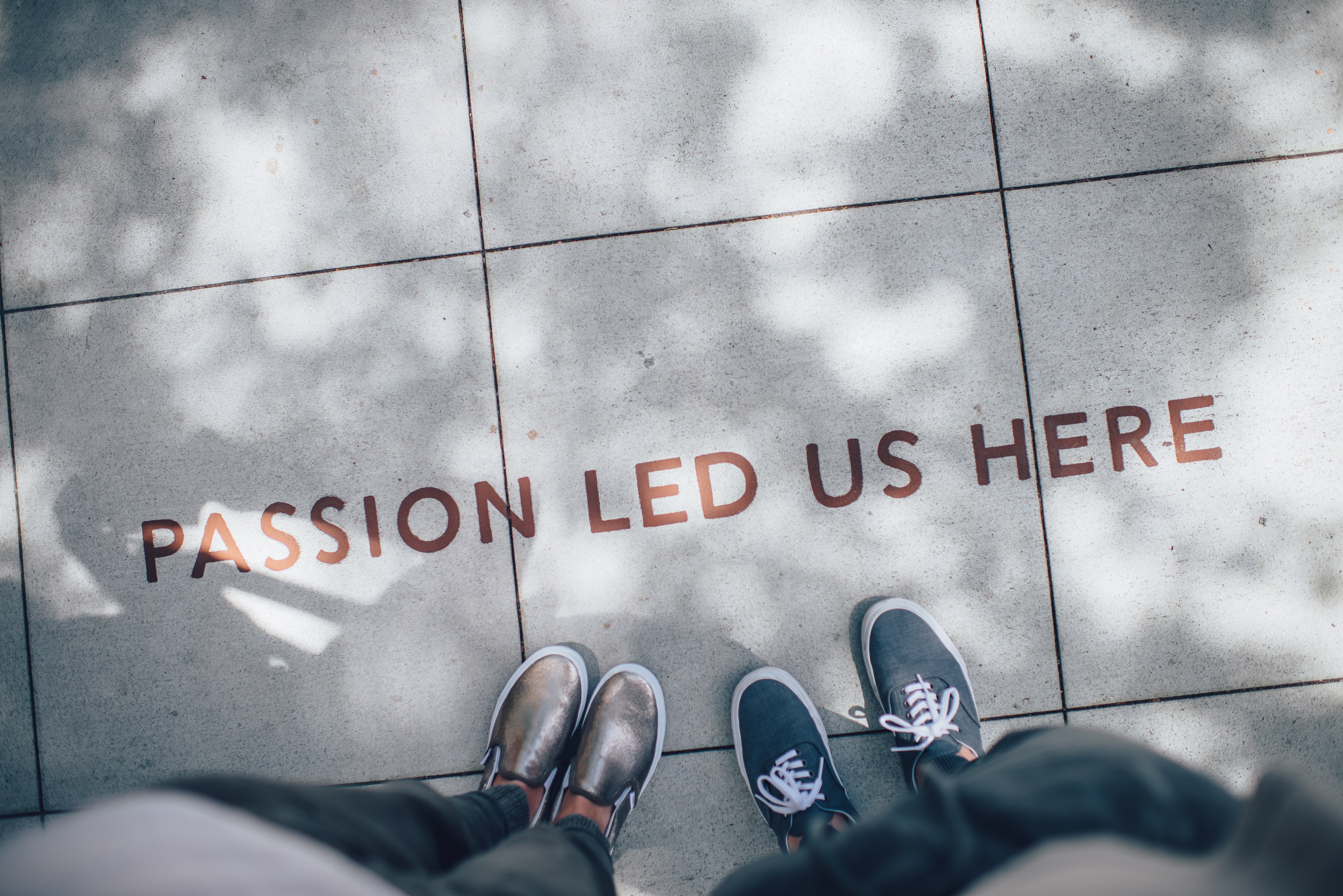Two pairs of shoes standing on pavement with the text 'PASSION LED US HERE'.