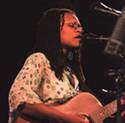 Woman singing and playing guitar on stage with microphone.
