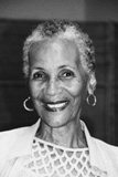 Portrait of a smiling elderly woman with short curly hair and hoop earrings.