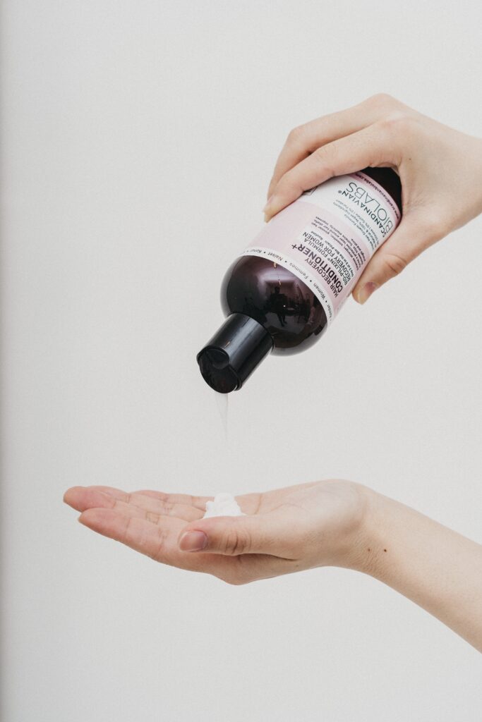 Person pouring liquid from a brown bottle onto hand.
