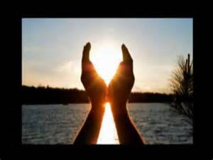 Hands framing the sun during a sunset over a body of water.