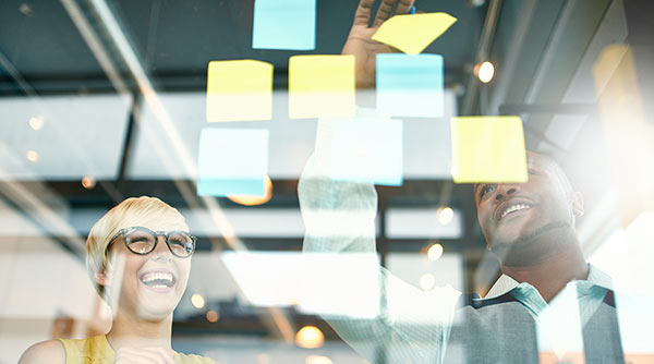 Team members brainstorming using sticky notes on glass wall.