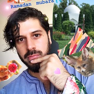 Man with beard and cat, colorful flags in the background.